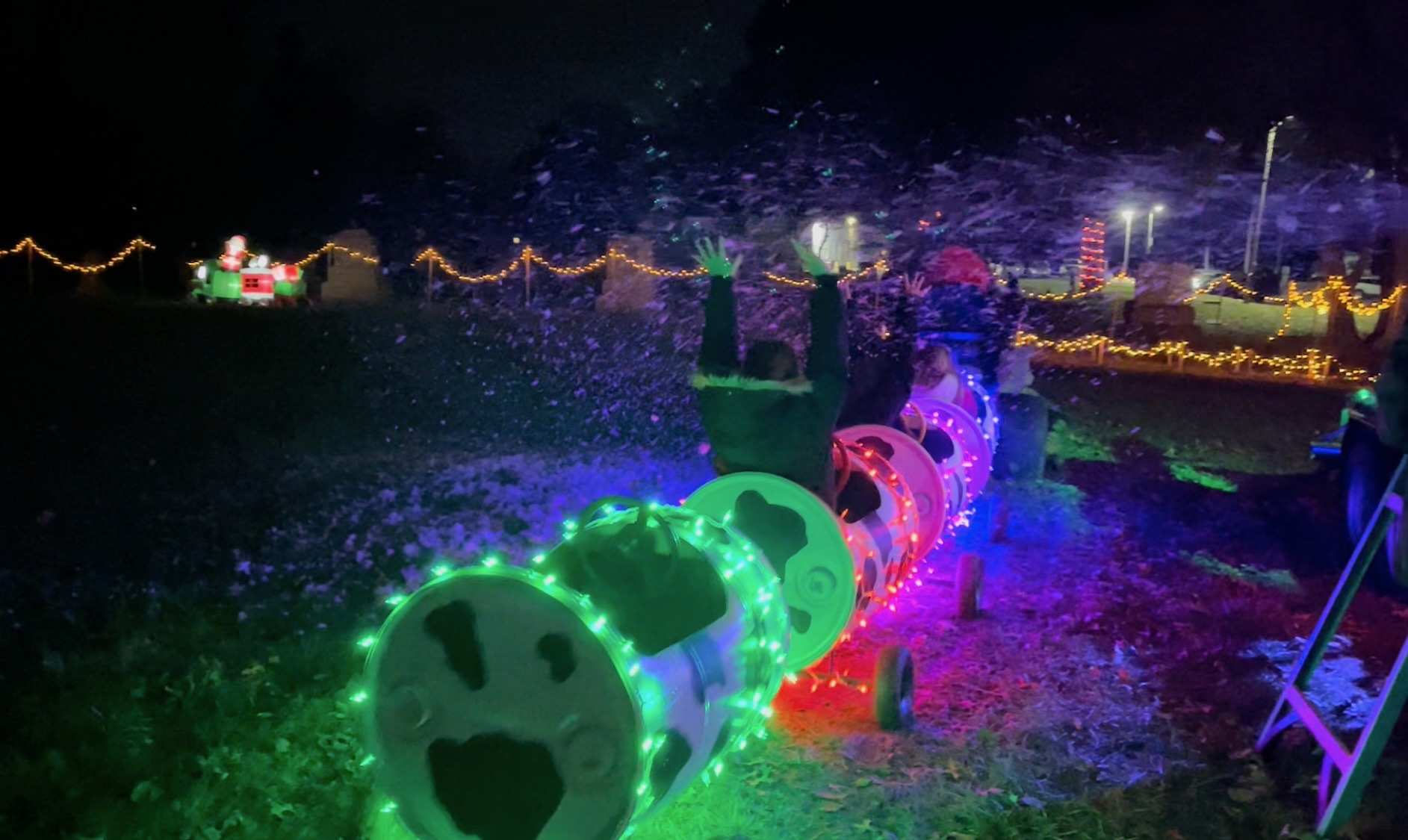 Children riding the lighted barrel cart train through falling snow